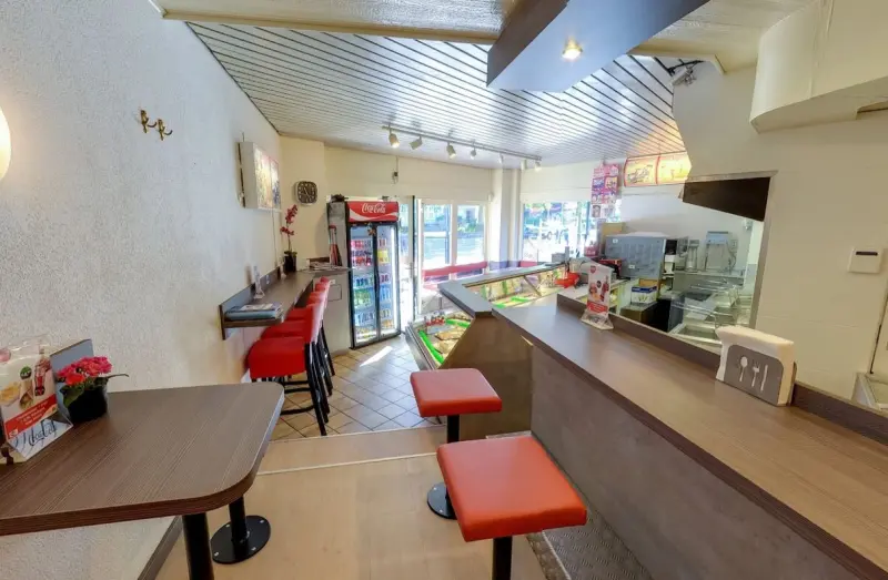 Zithoek achterin de zaak met houten tafel en rode krukken, met zicht op de toonbank